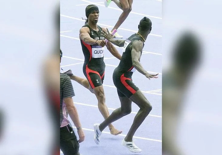 ONE SHORT: Renny Quow, left, hands the baton to his Trinidad and Tobago teammate Jereem “The Dream” Richards in the first of two Olympic Games men’s 4x400 metres qualifying round heats at the Stade de France, in Paris, yesterday. Quow, running the lead-off leg for T&T, lost his right shoe during the race. —Photo: BRENT STUBBS (Image obtained at trinidadexpress.com)